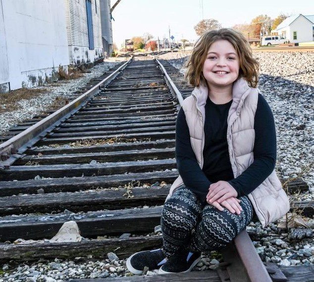 a cute little girl sitting on a railway track